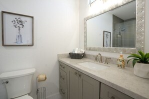 A bathroom with a toilet, sink, mirror, and framed artwork.