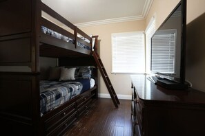 A bedroom with a bunk bed, a desk, and a window with blinds.