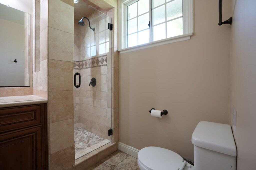 A bathroom with a shower, toilet, and a window.