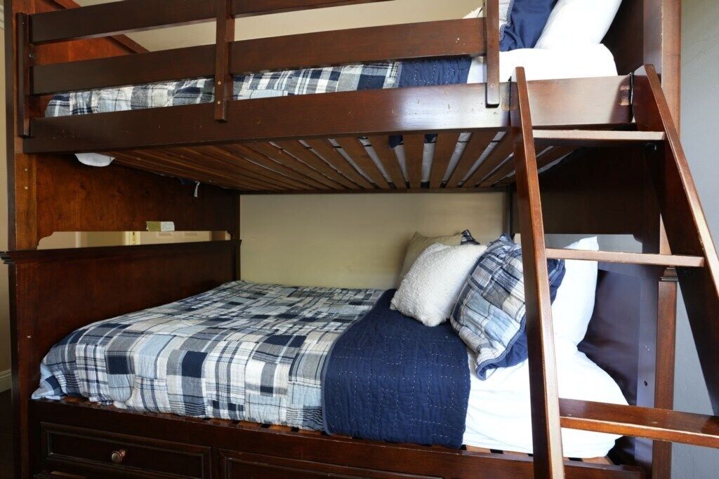 A bunk bed with a wooden frame, a plaid bedspread, and a white pillow.
