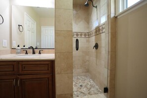 A bathroom with a shower, a sink with a mirror, and wooden cabinets.
