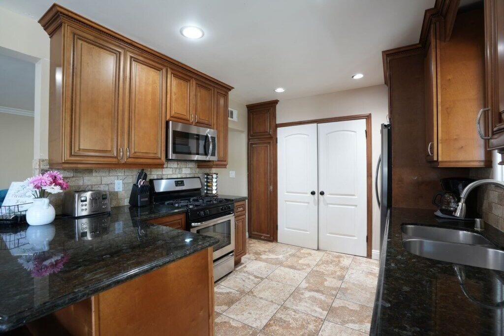 A kitchen with wooden cabinets, a stainless steel microwave, a stove, and a sink.