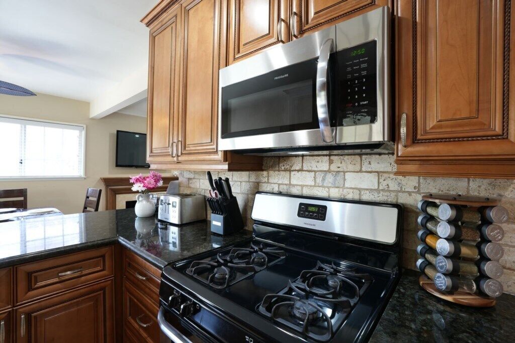 A kitchen with wooden cabinets, a stainless steel microwave, a gas stove, and a spice rack.