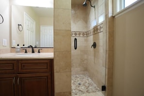 A bathroom with a shower, a sink with a mirror, and wooden cabinets.