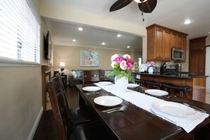 A dining area with a long wooden table set for four, a ceiling fan, and wooden cabinets in the background.