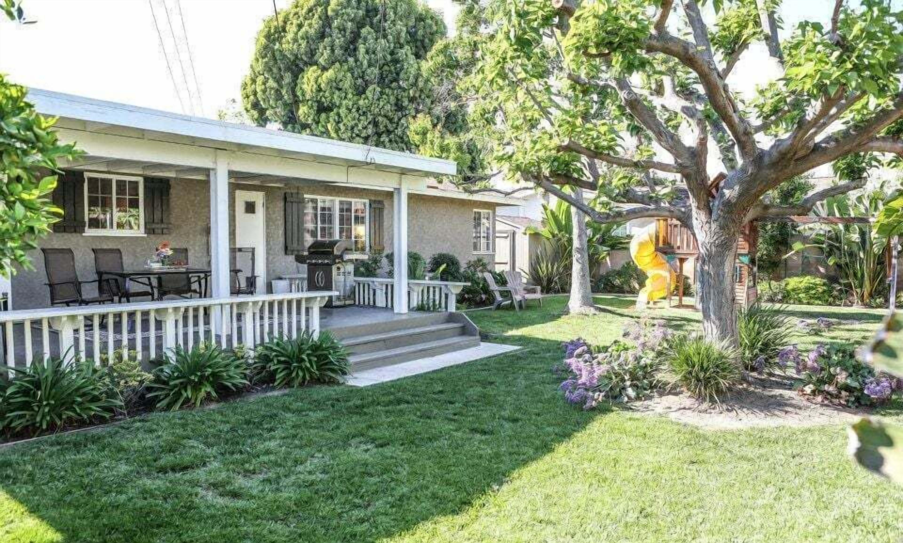 A house with a covered porch, outdoor seating, and a garden with a tree and plants.