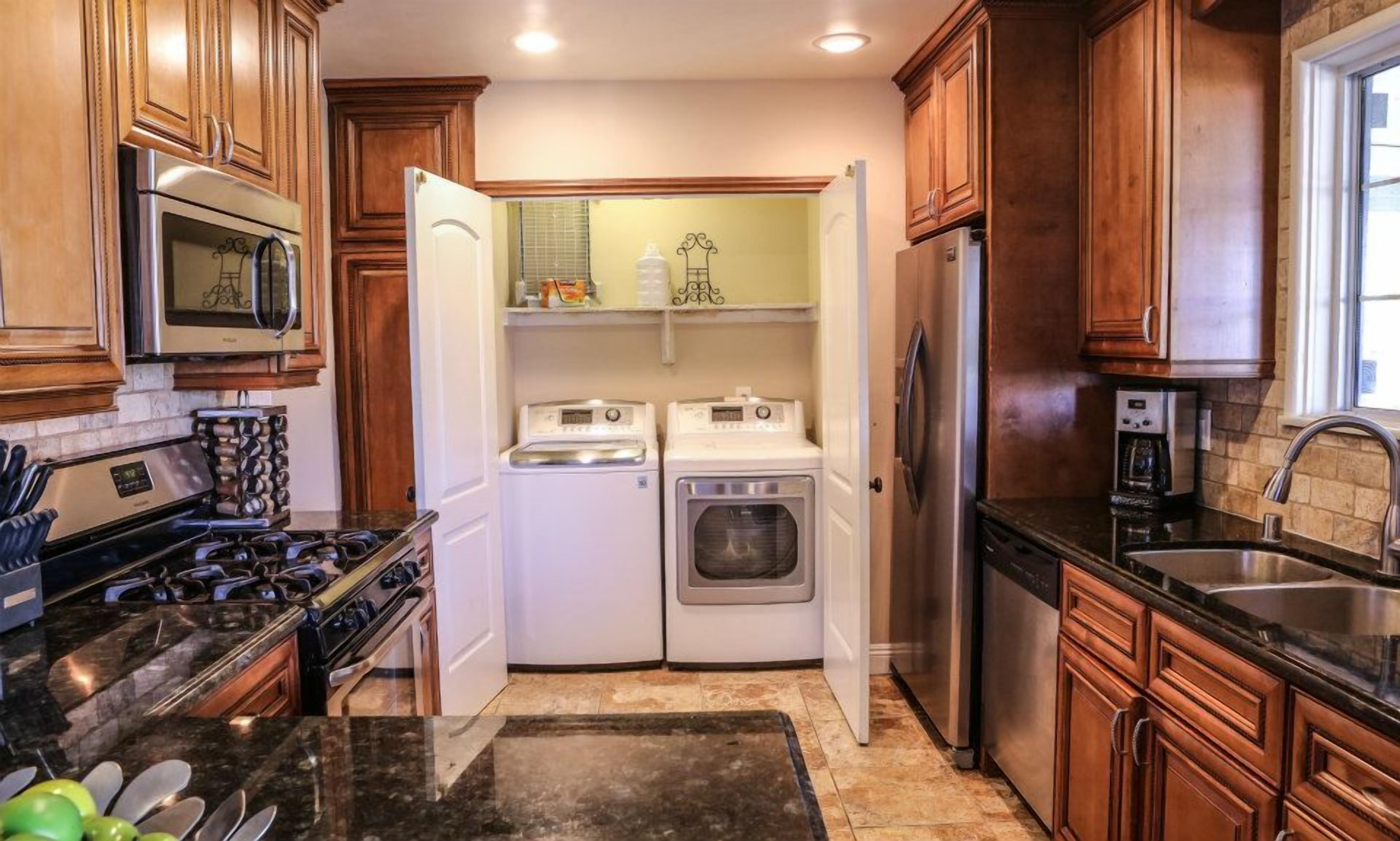 A compact kitchen with wooden cabinets, a microwave, a stove, a refrigerator, and a washing machine.