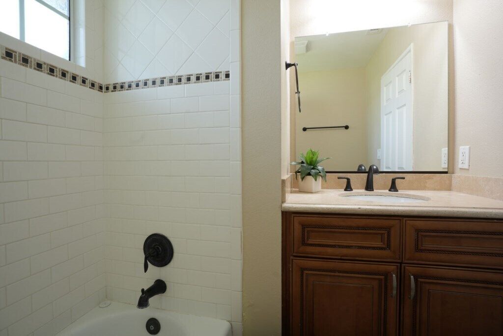 Un baño con paredes de azulejos blancos, una bañera, un lavabo con espejo y armarios de madera.