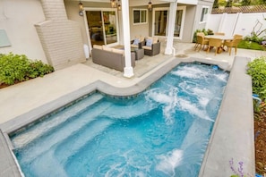 Una piscina con hidromasaje, mobiliario de exterior y un patio cubierto.