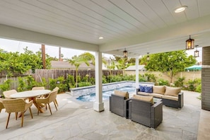 Un patio exterior con un jacuzzi, mobiliario de mimbre y vistas al jardín trasero.