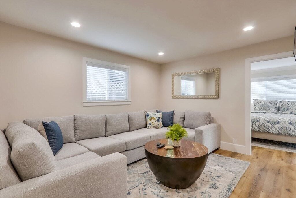 A living room with a sectional sofa, a round coffee table, and a mirror on the wall.