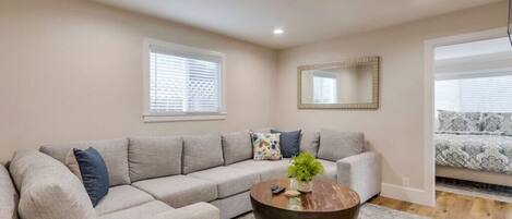 A living room with a sectional sofa, a round coffee table, and a mirror on the wall.