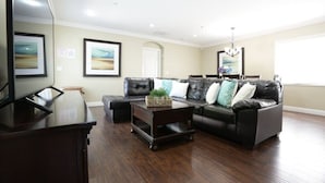 A living room with a dark wood coffee table, a black leather sofa with cushions, a television, and framed artwork on the walls. - Classy 4 Bedroom 3 Bath Pool Home 3/4 Mile Walk To Disney (Anaheim)