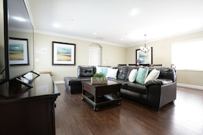 A living room with a dark wood coffee table, a black leather sofa with cushions, a television, and framed artwork on the walls. - Classy 4 Bedroom 3 Bath Pool Home 3/4 Mile Walk To Disney (Anaheim)