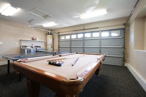 Una mesa de billar, una mesa de ping pong y una mesa de carambola en una sala con puerta de garaje.