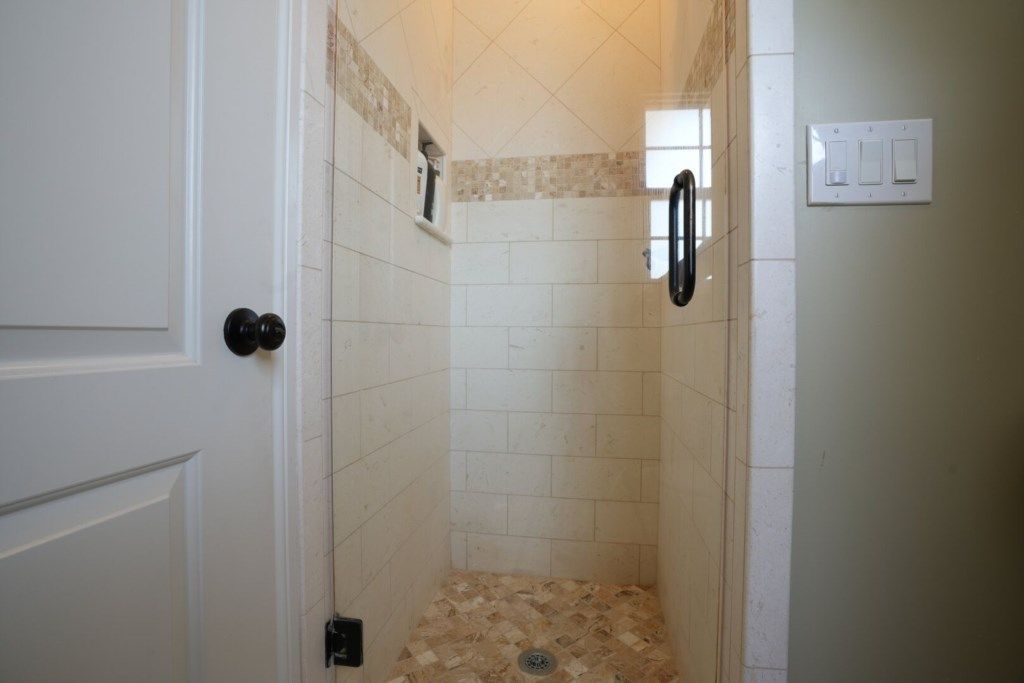 A small, enclosed shower area with tiled walls and floor, a door, and a light switch on the wall.