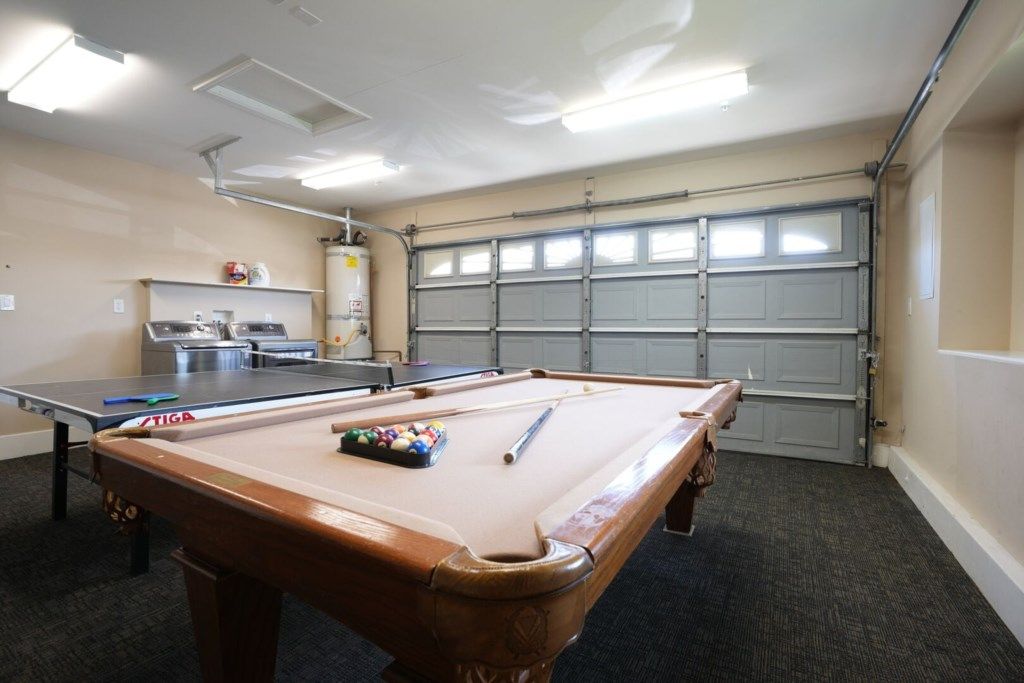 Una mesa de billar, una mesa de ping pong y una mesa de carambola en una sala con puerta de garaje.