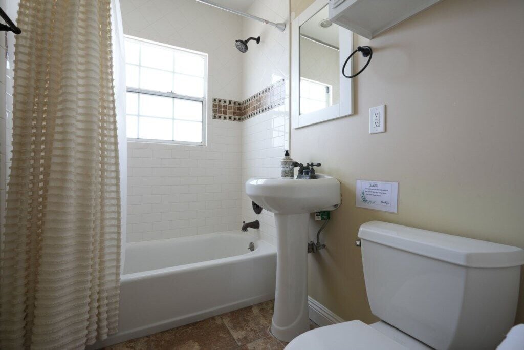 Ein Badezimmer mit Badewanne, Waschbecken, Toilette, Fenster und Spiegel.