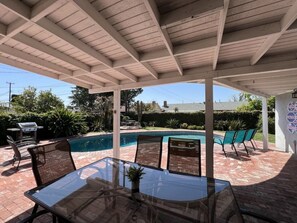 A covered patio area with a pool, outdoor furniture, and a grill.