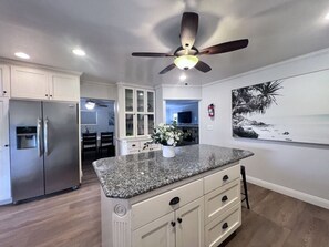 A kitchen with a granite countertop, white cabinets, a ceiling fan, and a painting of a beach scene. - Anaheim California, Beautiful Pool Home, Short Walk to Disney (Anaheim)