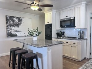 A kitchen with white cabinets, a granite countertop island, a ceiling fan, and a black microwave. - Anaheim California, Beautiful Pool Home, Short Walk to Disney (Anaheim)
