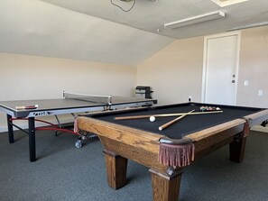 A pool table with a cue stick and billiard balls, a ping pong table, and a printer in a room with carpeted flooring and a door in the background. - Anaheim California, Beautiful Pool Home, Short Walk to Disney (Anaheim)