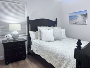 A bedroom with a bed, a nightstand, a lamp, and a wall-mounted picture. - Anaheim California, Beautiful Pool Home, Short Walk to Disney (Anaheim)
