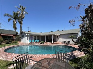 A swimming pool with a patio area, palm trees, and a covered section with chairs. - Anaheim California, Beautiful Pool Home, Short Walk to Disney (Anaheim)