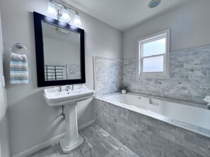 A bathroom with a pedestal sink, a bathtub, a window, and a mirror. - Anaheim California, Beautiful Pool Home, Short Walk to Disney (Anaheim)
