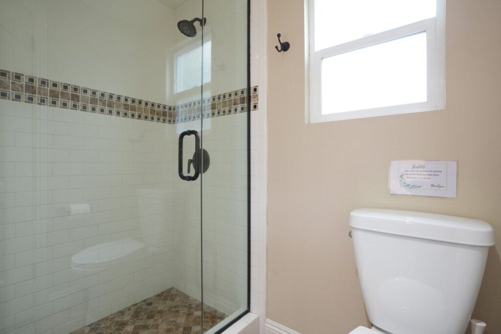 Une salle de bain avec une douche à parois de verre, des toilettes blanches et une petite fenêtre.