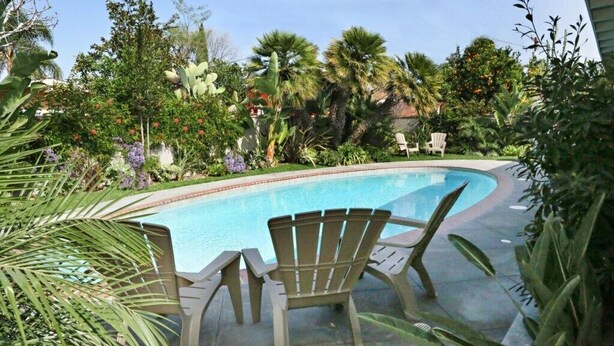 A swimming pool with two Adirondack chairs, surrounded by tropical plants and trees. - Comfy Pool Home,1/4 Mile Walk To Disneyland (Anaheim)