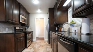 A kitchen with dark wooden cabinets, a stainless steel dishwasher, and a granite countertop. - Comfy Pool Home,1/4 Mile Walk To Disneyland (Anaheim)