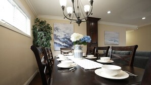 A dining room with a dark wooden table set for four, surrounded by chairs, a chandelier, and artwork on the walls. - Comfy Pool Home,1/4 Mile Walk To Disneyland (Anaheim)