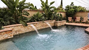 A swimming pool with a brick waterfall feature, surrounded by lush tropical plants and outdoor seating. - Wonderful 4 Bedroom 3 Bath Pool Home 3/4 Mile To Disney (Anaheim)