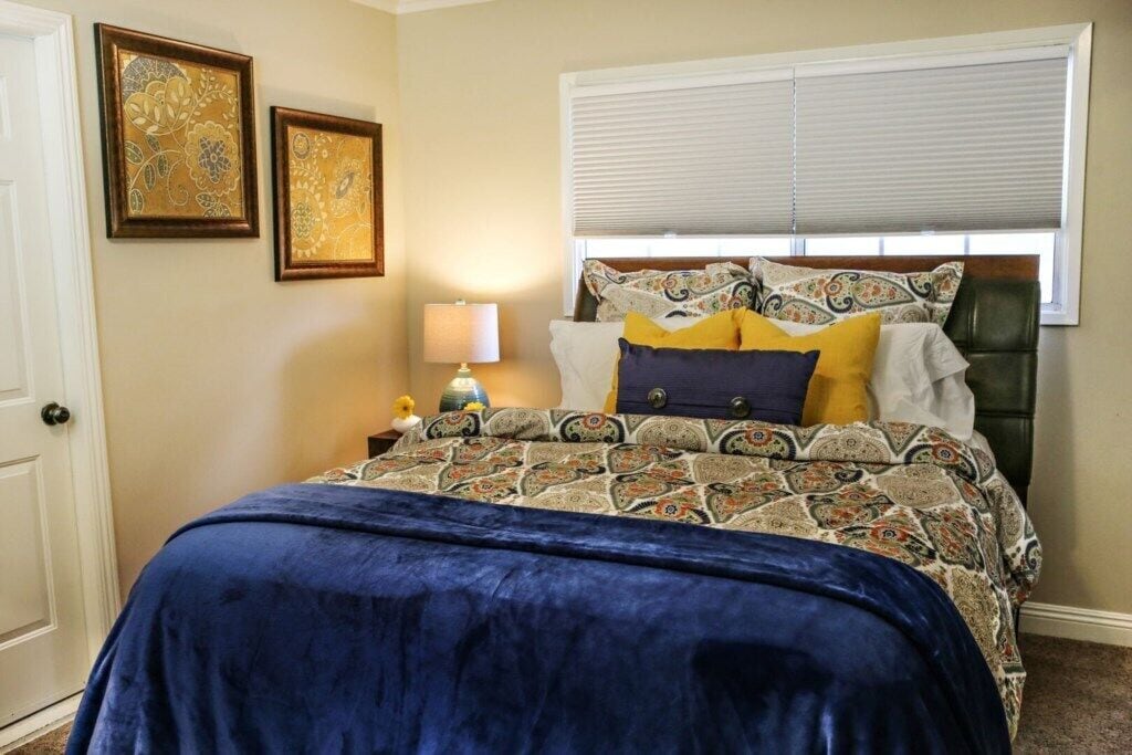 A bedroom with a bed, a nightstand, a lamp, and two framed pictures on the wall.