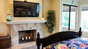 A bedroom with a fireplace, a bed with a floral bedspread, a television mounted above the fireplace, and a potted plant. - Wonderful 4 Bedroom 3 Bath Pool Home 3/4 Mile To Disney (Anaheim)