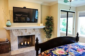Un dormitorio con chimenea, una cama con cubrecama floral, un televisor sobre la chimenea y una planta en maceta.