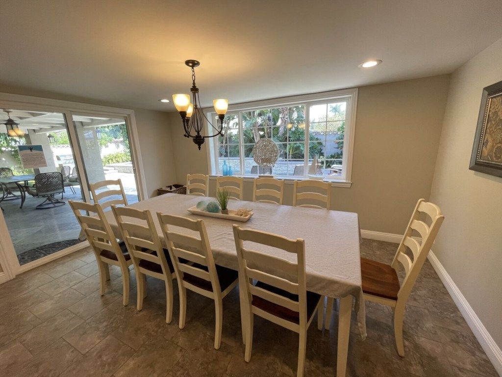 A dining area with a table and chairs, a chandelier, and a view through large windows.