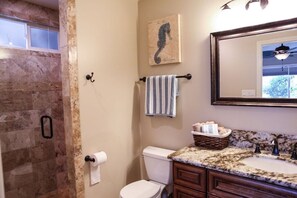 A bathroom with a marble sink, a toilet, a towel rack with a striped towel, a seahorse artwork, and a ceiling fan.