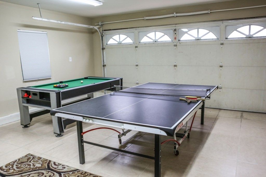 A room with two ping pong tables, a pool table, and a window with blinds.