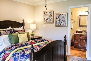 A bedroom with a bed, nightstand, wall art, and a view into the bathroom.