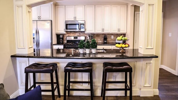 A kitchen with white cabinets, a stainless steel refrigerator, a microwave, a stove, and a central island with stools. - Wonderful 4 Bedroom 3 Bath Pool Home 3/4 Mile To Disney (Anaheim)