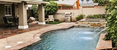 A backyard with a swimming pool, patio furniture, and a barbecue area.