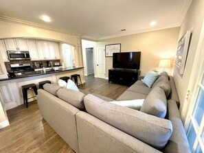 Una sala de estar con un sofá modular, un televisor de pantalla plana y una cocina con electrodomésticos modernos.