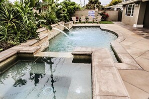 A swimming pool with a waterfall feature, surrounded by a stone wall and various plants.
