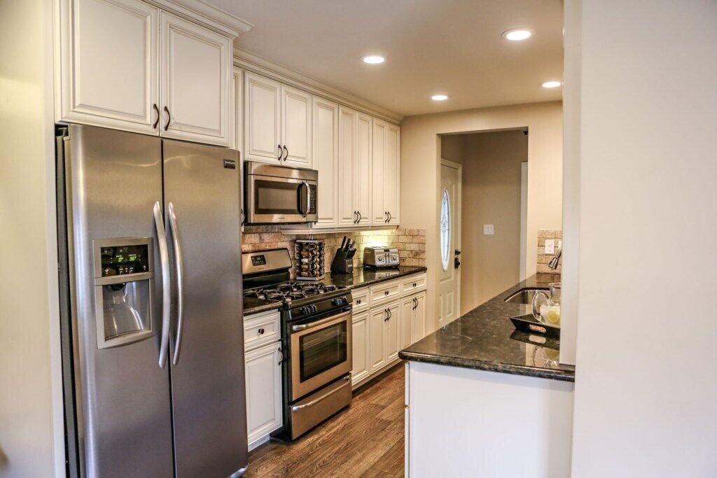 A modern kitchen with stainless steel appliances, white cabinetry, and a granite countertop.