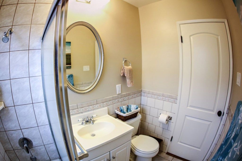 A bathroom with a shower, sink, toilet, and a mirror.