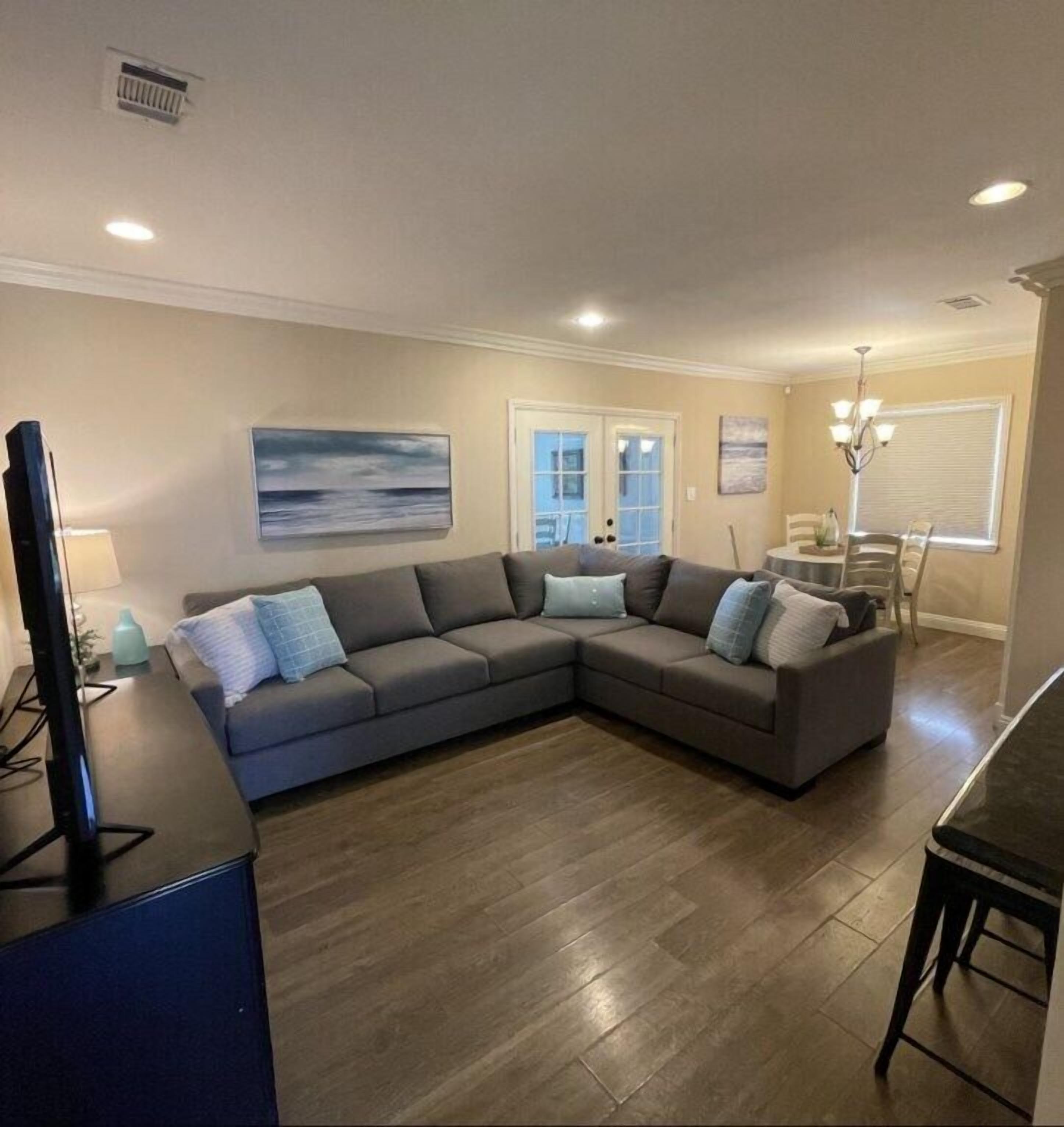 A living room with a sectional sofa, a flat-screen TV, and a dining area with a chandelier.