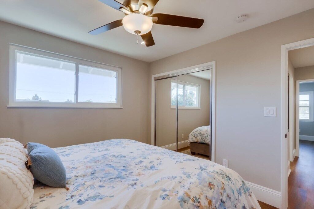 A bedroom with a bed, a ceiling fan, a large window, and a closet.