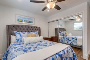 A bedroom with a large bed, a ceiling fan, a mirror, and a painting on the wall. - Gorgeous Upgraded 5 Bedroom & 3 Bath Home with pool (Santa Ana)